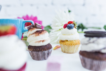 Cupcakes with fresh berries flowers and leaves, a cup of tea or coffee.