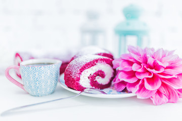 A red velvet cake roll sliced with cup of coffee or tea and flowers.