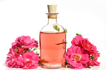 Rose Water in glass bottles  with pink roses on white background with reflection. Massage, aromatherapy and organic cosmetics concept