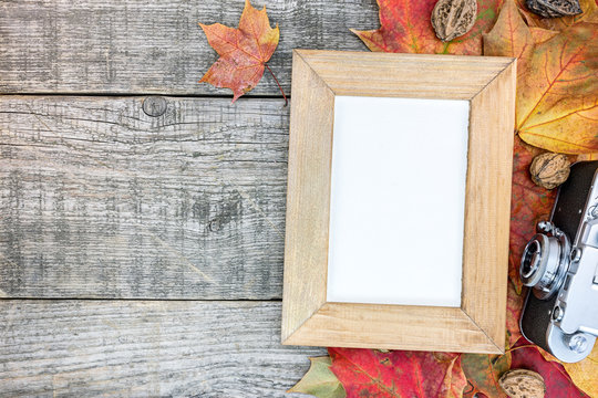 grunge wooden background with vibrant withered autumn leaves, retro camera and photo frame