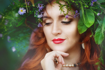 Close-up portrait of a redhead woman with a wreath of flowers on her head and hand at chin