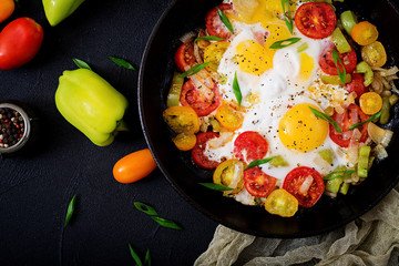 Fried eggs with vegetables - shakshuka in a frying pan on a black background. Flat lay. Top view