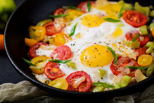 Fried eggs with vegetables - shakshuka in a frying pan on a black background