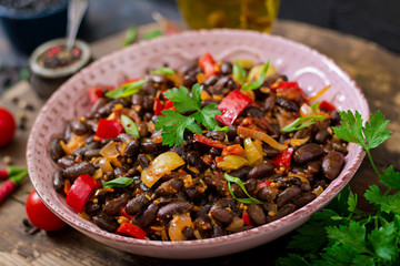 Stewed black beans with sweet peppers and tomatoes with spicy sauce in a pink bowl