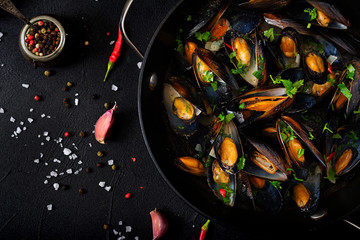 Mussels cooked in wine sauce with herbs in a frying pan on a black background. Flat lay. Top view.