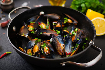 Mussels cooked in wine sauce with herbs in a frying pan on a black background.