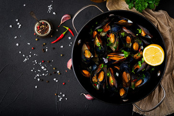 Mussels cooked in wine sauce with herbs in a frying pan on a black background. Flat lay. Top view.