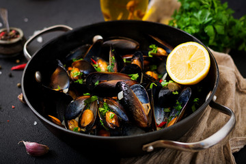 Mussels cooked in wine sauce with herbs in a frying pan on a black background.