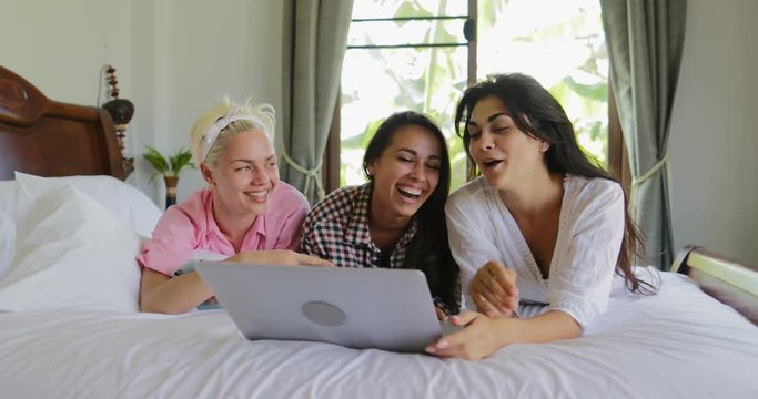 Girls Using Laptop Computer Lying On Bed Laugh Talking, Young Women Group Communication In Bedroom Slow Motion 60