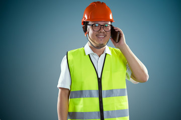 Young asian construction workers in safety helmet and using smartphone, isolated on blue background