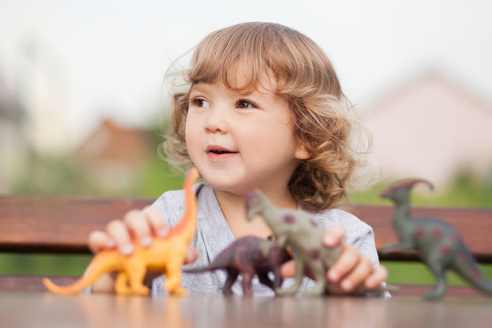 Toddler kid playing with a toy dinosaurs outdoors.