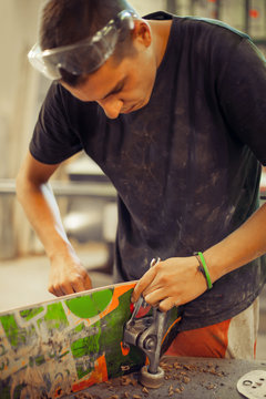 Young man in carpentry workshop fixing wheel on his skateboard