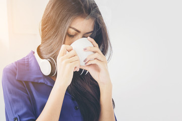close up of pretty woman relaxing with music by headphone and drinking coffee beside window in the morning