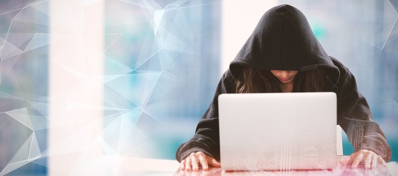 Composite image of female hacker sitting by laptop on table 