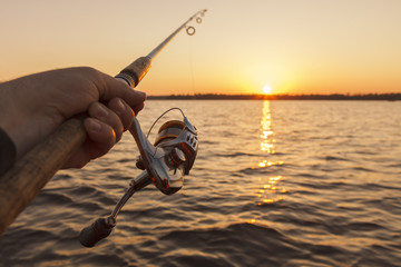 fishing rod in hand on sunset background