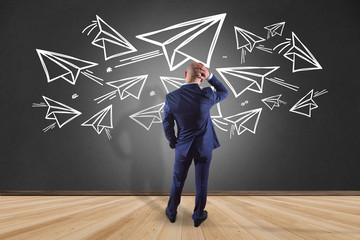 Businessman in front of a wall watching paper planes - Travel concept