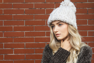 Portrait of a beautiful blonde woman wearing a large warm winter hat. Nice background of this composition is created of red brick wall.
