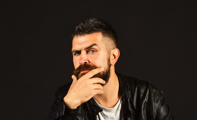 Man with beard wears black jacket. Guy with suspicious face
