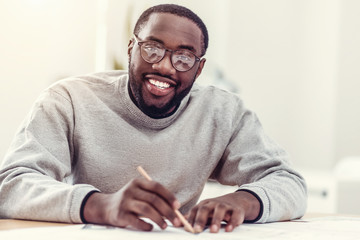 Beaming African American guy drawing and smiling into camera
