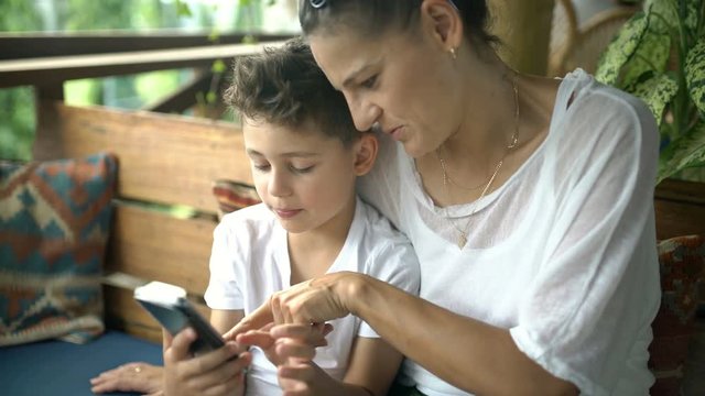 Son sitting with his mother and browsing internet on smartphone, steadycam shot
