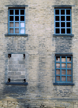 four broken and bricked up windows in a derelict abandoned old house with dirty stained bricks