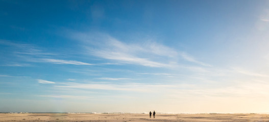 Couple wealking on an open, unpopulated beach. All alone.