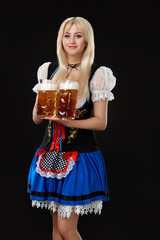 Young sexy woman wearing a dirndl with two beer mugs on black background.