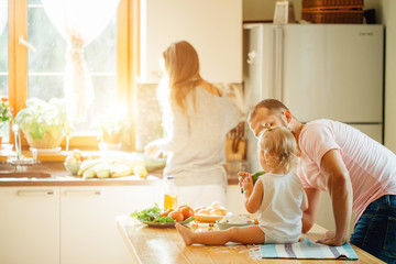 Young couple with kid having fun in the kitchen while preparing vegetable salad