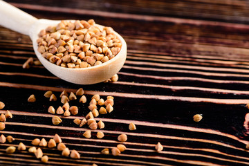 Buckwheat raw seeds in wooden spoon on wood table. Healthy eating background