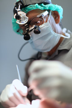 dental surgeon with mask and magnifying glasses doing an operation, dental implant