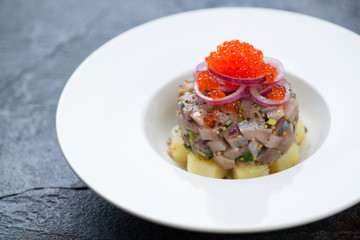 White plate with herring fillet tartar on a grey stone background, horizontal shot, selective focus
