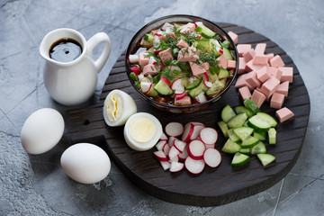 Traditional russian cold soup okroshka with some of its cooking components on a black wooden chopping board, studio shot