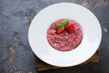Strawberry risotto served in a white plate on a brown stone background