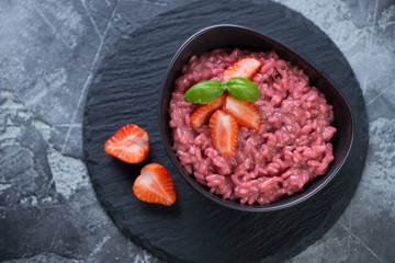 Risotto with strawberries served in a bowl on a stone slate, above view, studio shot