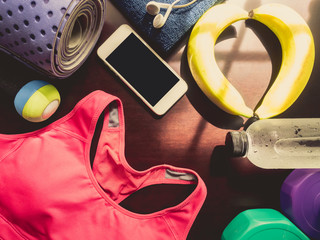 gym workout accessory from sportswear , yoga mat , dumbbell and refresh energy by banana and relax by listen music with earphones and smart phone with soft focus shadow on wood background