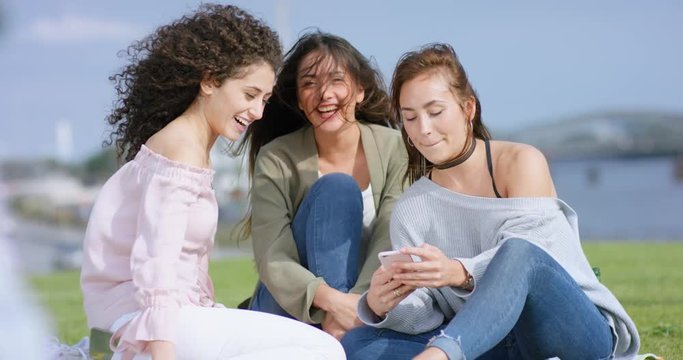 Beautiful girlfriends sitting outside with smartphone and flirting