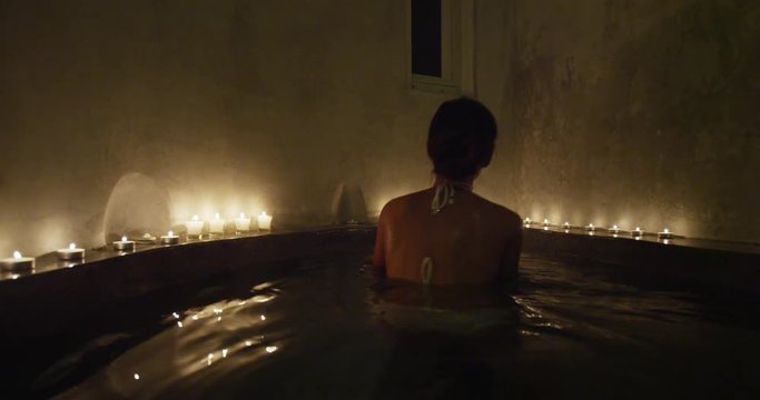 Happy asian bikini woman entering jacuzzi hot tub pool swimming in warm soothing water relaxing at spa resort hotel outdoor terrace. Lady enjoying night in relaxation candlelit room at health center.