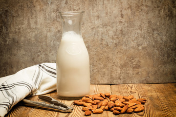 Leche de almendras en botella y almendras naturales sobre mesa de madera. Vista de frente. Copy space