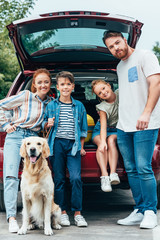 family with dog standing next to car