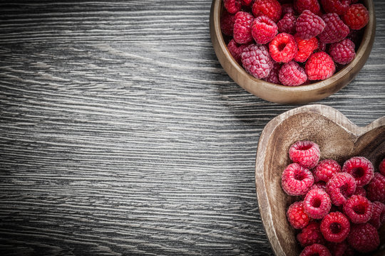 Round and heart-shaped bowls with red raspberries on wooden boar