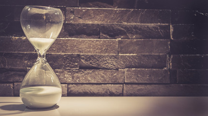 Broken hourglass, sand clock on a dark gray brick wall background