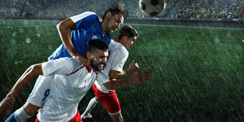 Obraz premium Soccer players performs an action play on a professional rainy stadium. Two football teams fighting for the ball. Players wears unbranded sport uniform.