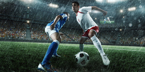 Soccer players performs an action play on a professional rainy stadium. Two football teams fighting for the ball. Players wears unbranded sport uniform.