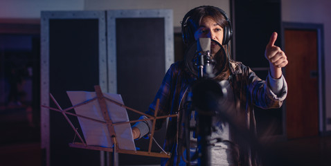 Female singer with thumbs up sign in recording studio