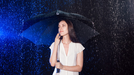Beautiful young woman with umbrella under rain, night