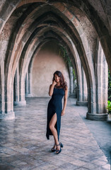Fototapeta na wymiar Fashion portrait of a young beautiful girl in black fashionable dress and black shoes on a neo-gothic terrace