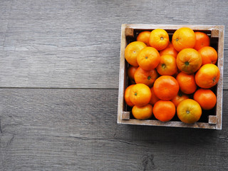 Fresh tangerines in an old box with leaves. On wooden background. Top view