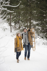 Happy young couple with sledge in winter forest