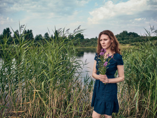 The red-haired girl in a blue summer dress strolls along the lake.