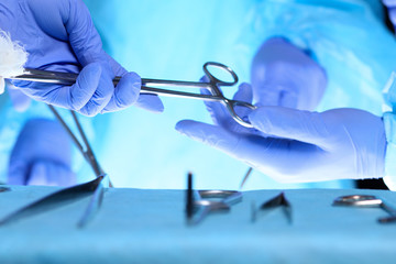 Surgeons hands holding surgical scissors and passing surgical equipment, close-up. Health care and veterinary concept